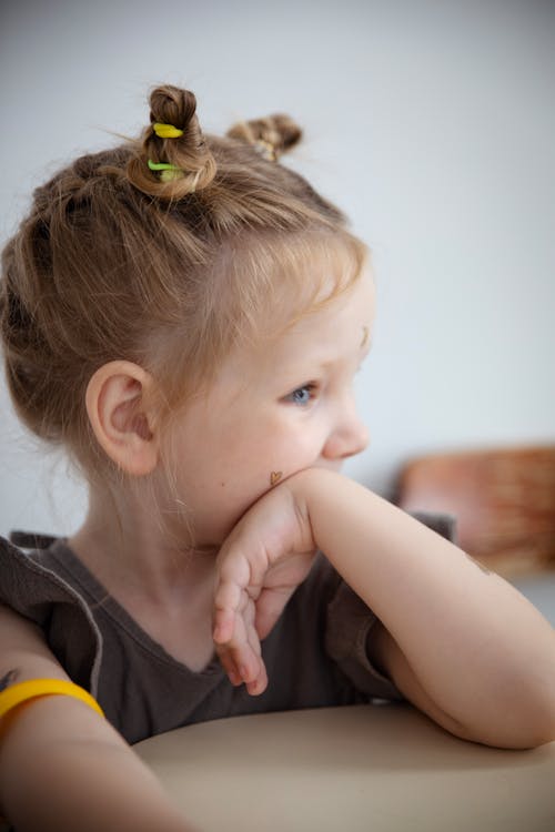 Free A thoughtful portrait of a young blonde girl with a unique hairstyle and hand on cheek. Stock Photo