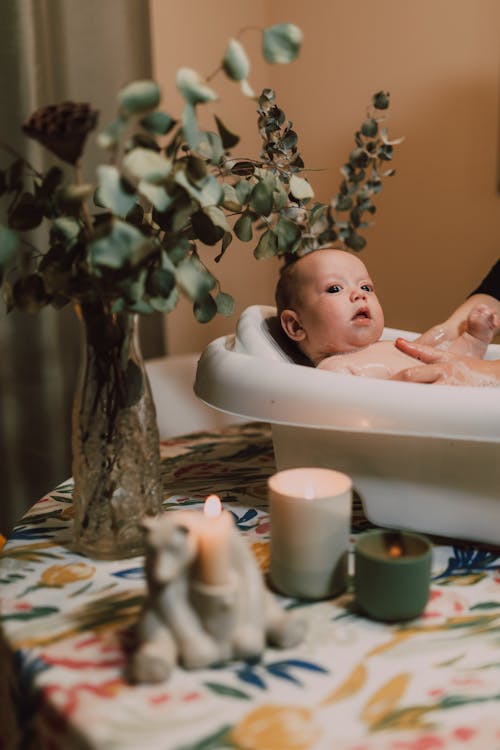 Free A cute baby in a tub surrounded by candles and greenery on a table indoors. Stock Photo