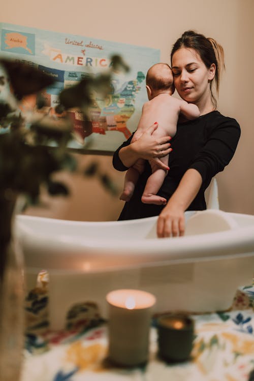 Free A mother lovingly holds her baby while preparing a bath in a warm, comforting environment. Stock Photo