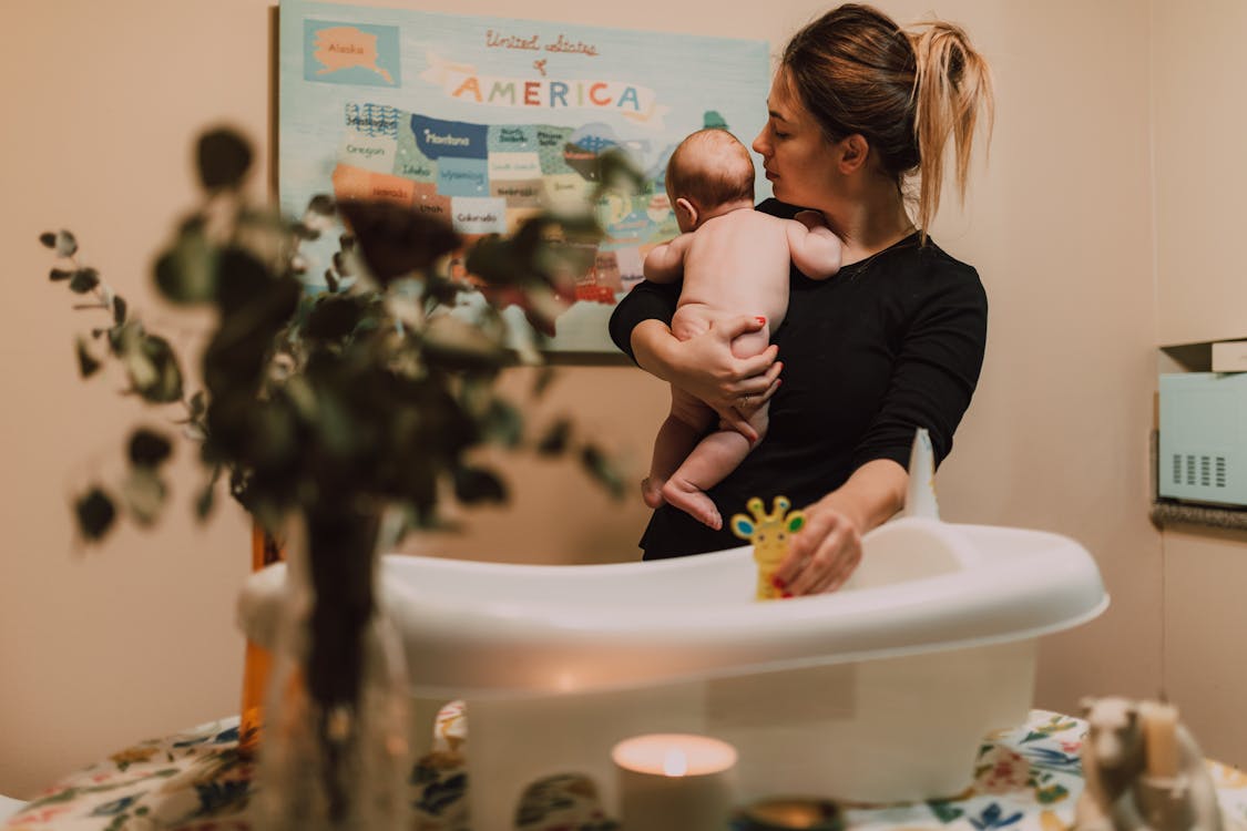 Free A mother lovingly holds her baby near a bath with a warm, intimate atmosphere. Stock Photo