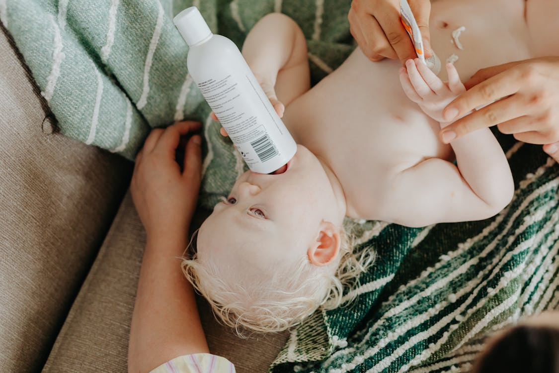 Free A cute baby lies comfortably while holding a lotion bottle during a skincare routine. Stock Photo