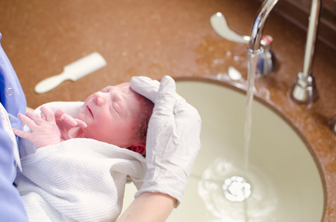 Free A nurse gently bathes a newborn in a hospital sink, ensuring care and hygiene. Stock Photo