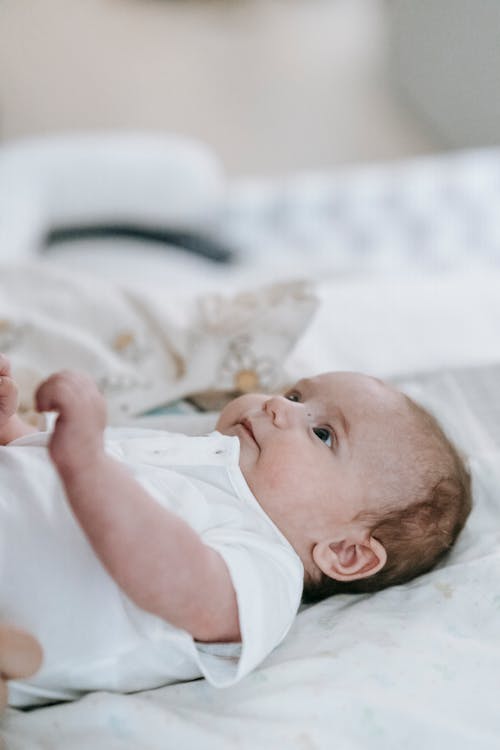 Free Sweet newborn baby in a white outfit lying comfortably on a bed, capturing a calm and peaceful moment at home. Stock Photo