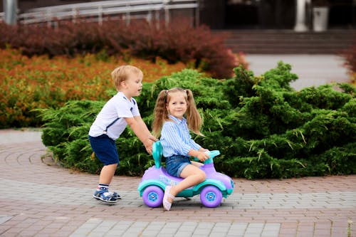 Free Boy Pushing a Girl Riding in Toy Car Stock Photo