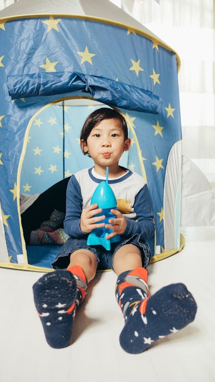 Free A Boy Holding a Drink Bottle Sitting on the White Floor Stock Photo