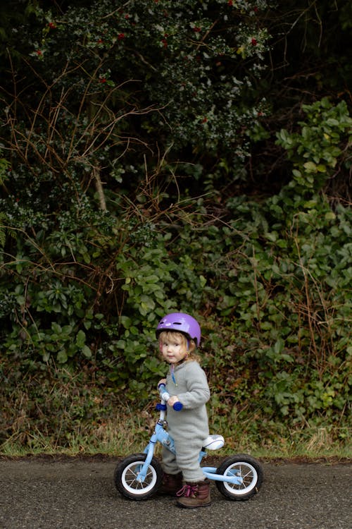 Free Adorable little girl riding bicycle on sidewalk against thickets of forest Stock Photo