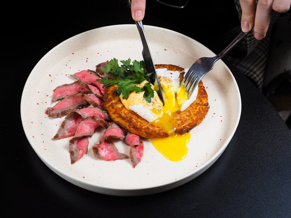 Free Delicious dish of sliced beef, runny egg, and herbs on a plate, perfect for food photography. Stock Photo