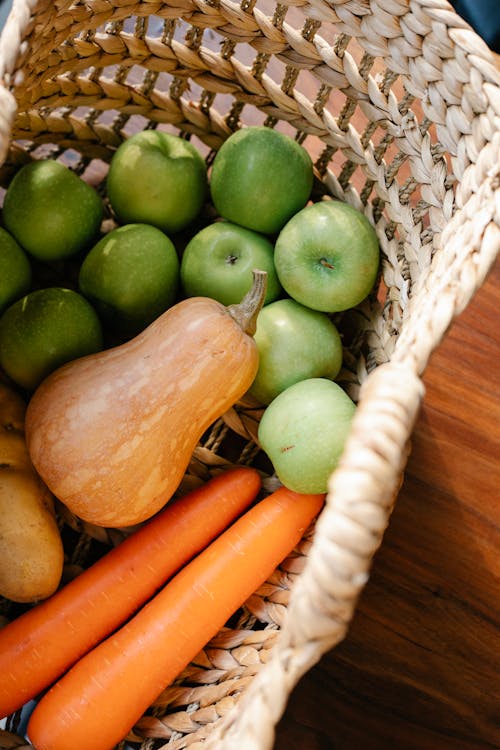 Free A wicker basket filled with fresh vegetables and fruits including apples, carrots, and a butternut squash. Stock Photo