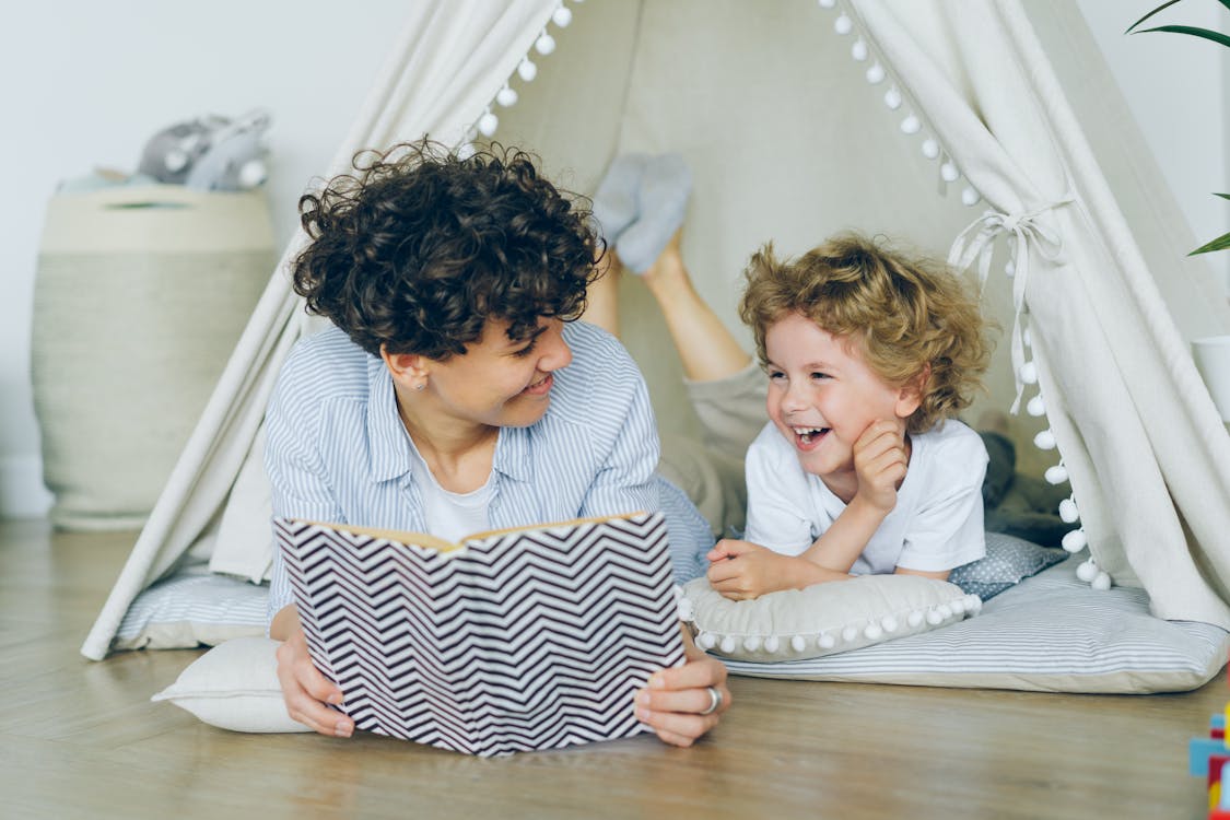 Free Mother Lying Down with Son in Tent and Reading Book Stock Photo