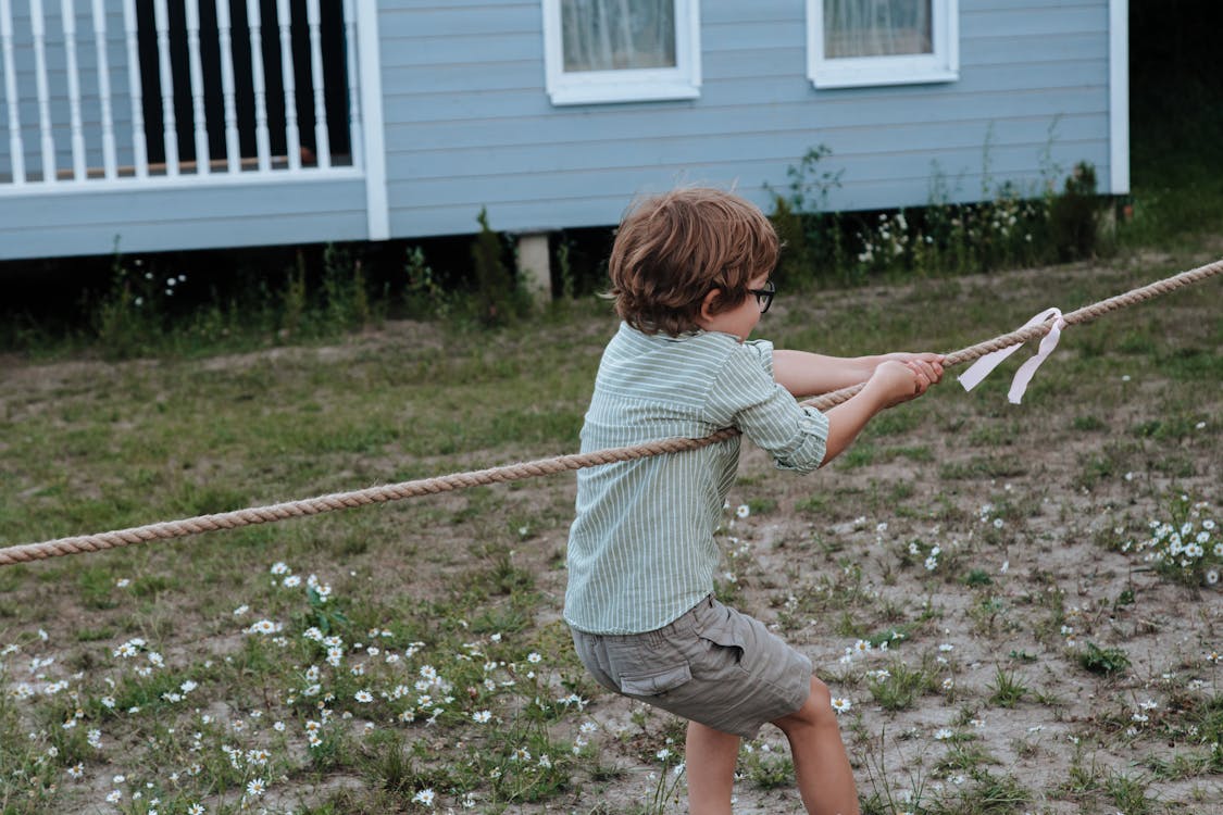 Free Young boy engaged in a tug of war outside near a blue building during the day. Stock Photo