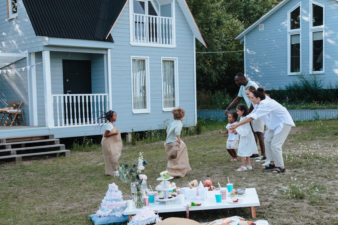 Free Children enjoying a sack race with parents cheering in a backyard garden. Stock Photo