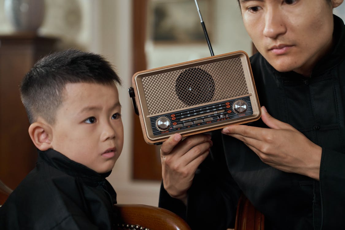 Free Father and son sharing a moment, listening to a vintage transistor radio indoors. Stock Photo