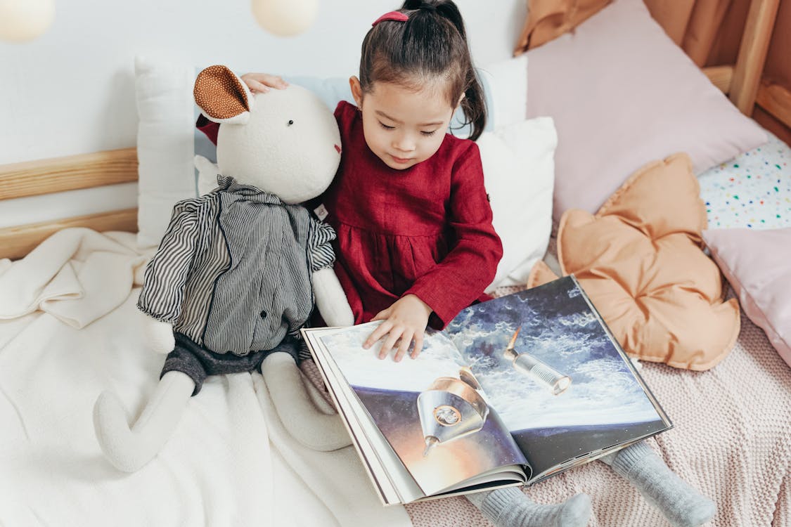 Free Girl in  Red Dress Sitting on Bed Reading Book Stock Photo