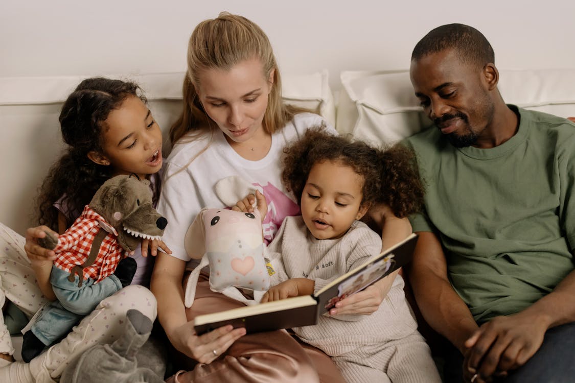 Free A diverse family enjoys reading a storybook together, fostering warmth and connection. Stock Photo