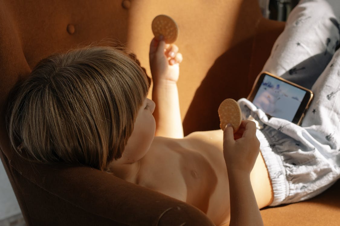 Free Topless Boy Lying on Sofa Chair While Holding Biscuits Stock Photo