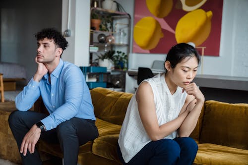 Free A couple sits indoors on a sofa, both appearing thoughtful and contemplative. Stock Photo